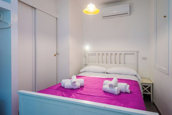 A bedroom with a bed, pillows, a nightstand, and a wall-mounted air conditioner. - Casa Fresta (Taormina)