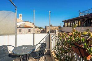 A balcony with a table and chairs, overlooking a cityscape with historic buildings and a clear blue sky. - Casa Fresta (Taormina)