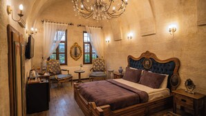 A bedroom with a large bed, two chairs, a small table, and a chandelier. - Yesil Konak Cave Hotel (Ürgüp)