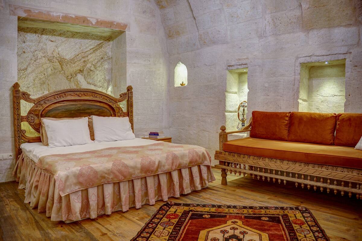 Una habitación con una cama de madera, un sofá, un tapiz estampado y paredes de piedra.