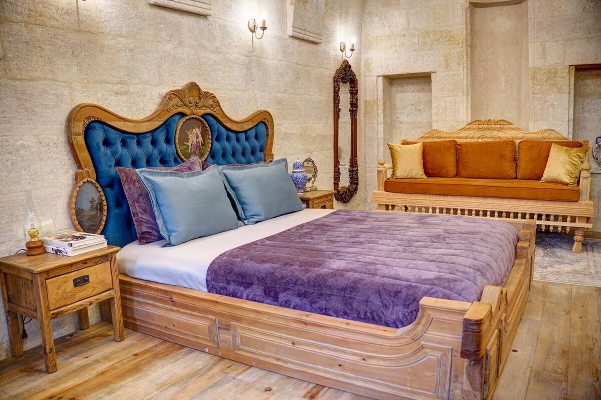 Un dormitorio con una cama grande, una mesita de noche de madera, un aparador, un espejo y un sofá.