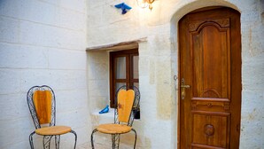 Two wooden chairs with metal frames and a wooden backrest, positioned outside a building with a stone wall and a wooden door. - Yesil Konak Cave Hotel (Ürgüp)