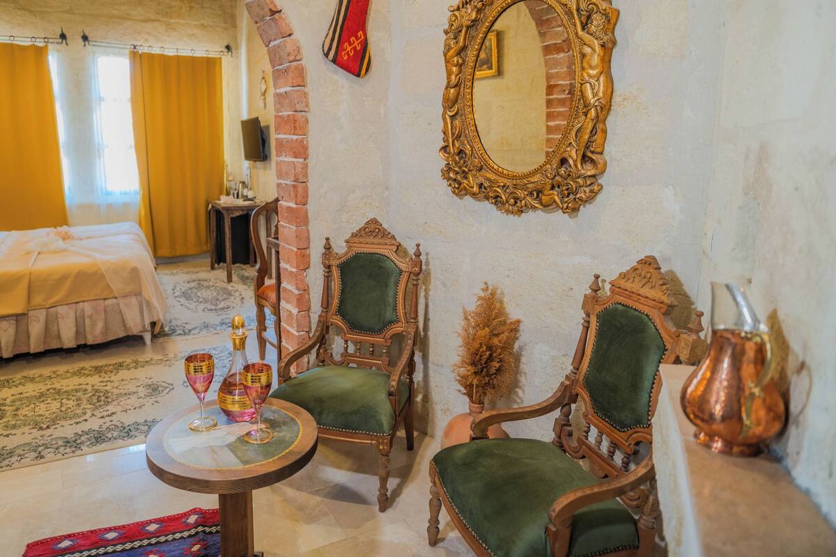 Una habitación tradicional con una cama, dos sillas decoradas, una mesita con vasos y un espejo en la pared.