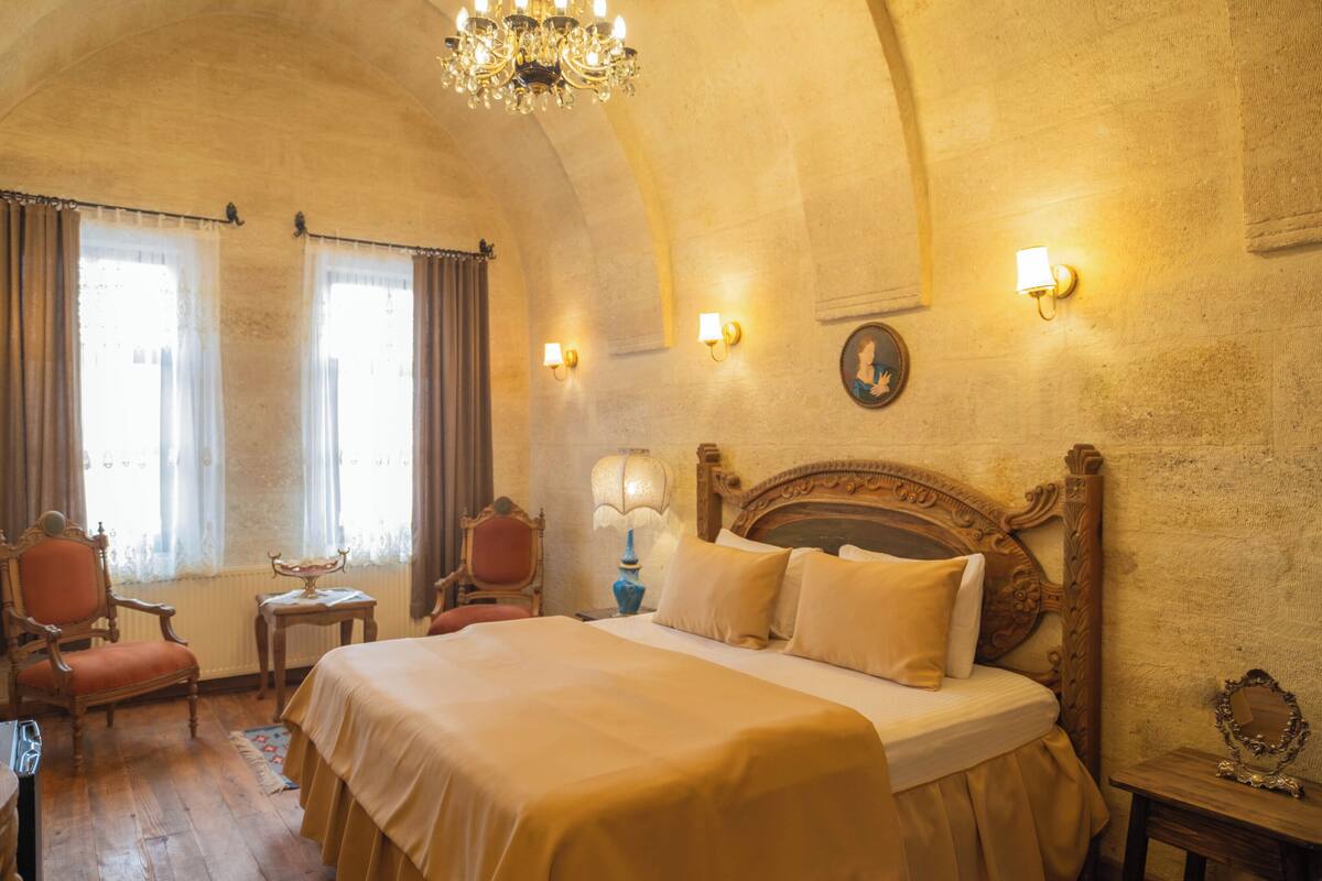 Una habitación con una cama grande, dos sillones, una mesa, una araña y apliques de pared.
