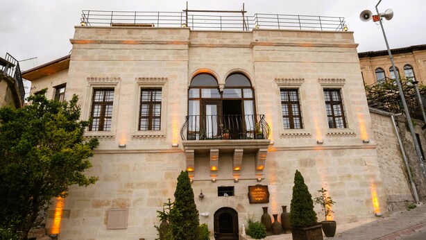 A historic building with a central entrance, arched windows, and a balcony with potted plants. - Yesil Konak Cave Hotel (Ürgüp)