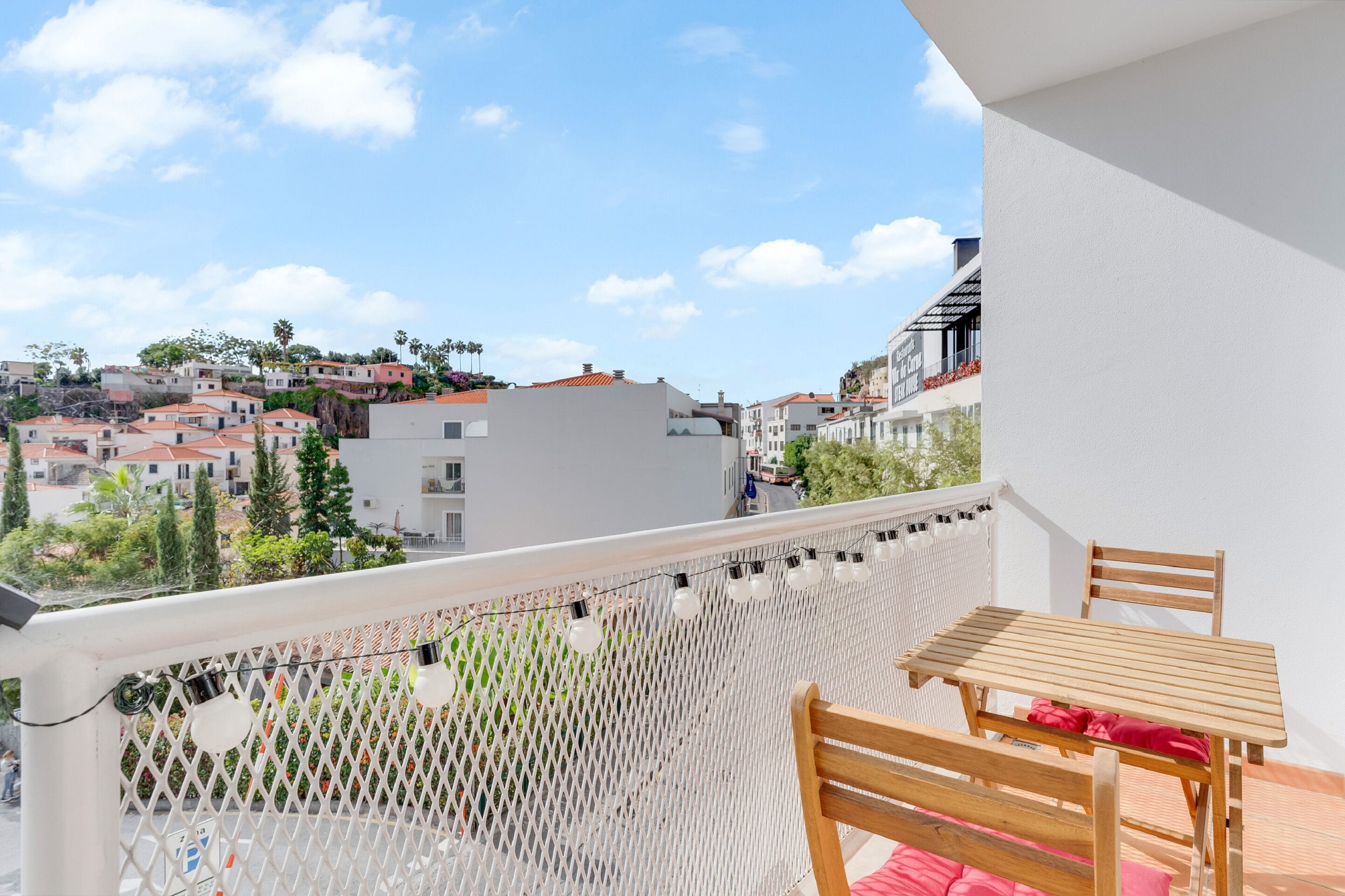 A balcony with a white railing, a wooden table, and a chair.