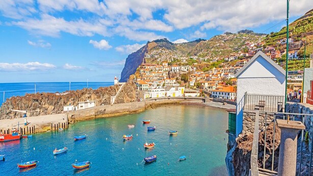 A coastal town with colorful boats docked at a pier, a lighthouse, and buildings on a hillside. - Camara de Lobos Apartment (Camara de Lobos)
