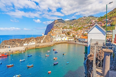 A coastal town with colorful boats docked at a pier, a lighthouse, and buildings on a hillside.