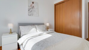 A bedroom with a bed, nightstands, a wooden wardrobe, and a wall art piece. - Camara de Lobos Apartment (Camara de Lobos)