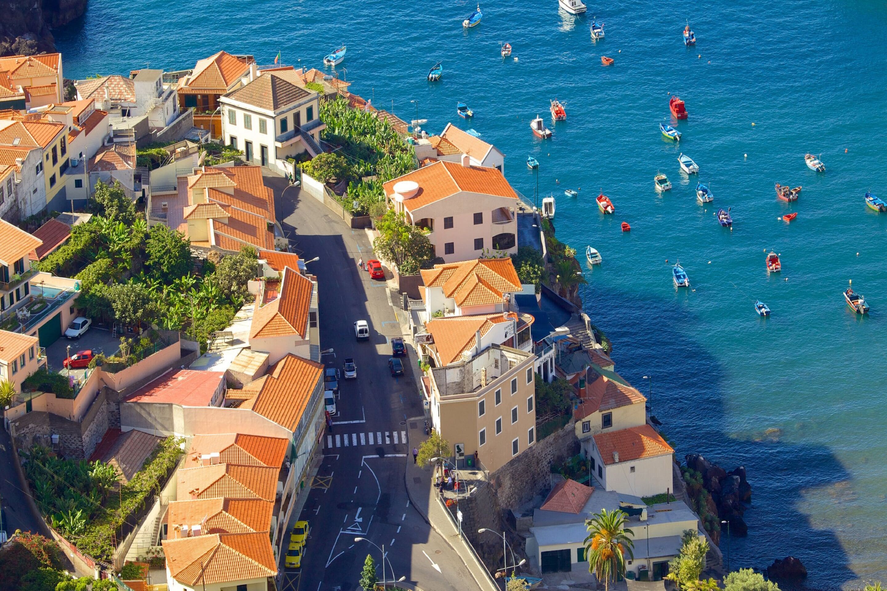 Eine Küstenstadt mit terrakottafarbenen Dächern, einer schmalen Straße und Booten auf dem Wasser.