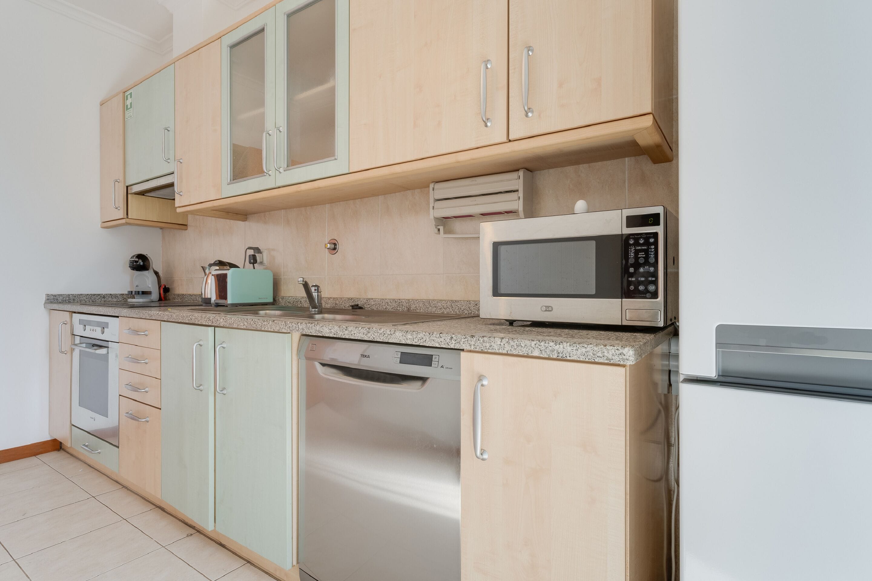 Eine moderne Küche mit hellen Holzschränken, einem integrierten Geschirrspüler, einer Mikrowelle und einem Edelstahlbackofen.
