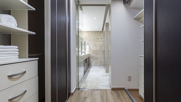 Un baño moderno con cabina de ducha de vidrio, pared con azulejos de mármol y suelo de madera.