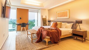 Un dormitorio moderno con una cama grande, mesitas de noche, un escritorio y vistas a la ciudad.