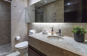 Ein modernes Badezimmer mit Marmorplatte, Waschbecken, Toilette, Dusche und einer Topfpflanze.