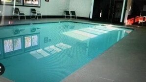 Une piscine à l’eau claire, entourée de chaises et bordée d’un mur carrelé.
