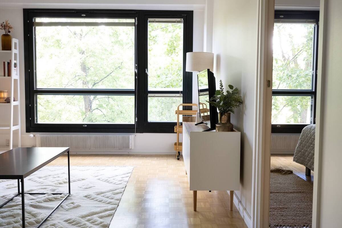 A modern room with large windows, a desk, a chair, a lamp, and a plant.