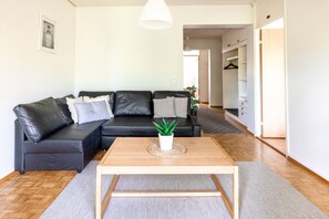 A modern living room with a black leather sofa, a wooden coffee table, and a potted plant. - 2ndhomes 2BR Center Apartment w Balcony (Helsinki)