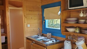 Puisesta hirrestä rakennettu keittiö, jossa on puinen pöytä, pesuallas, liesi ja mikroaaltouuni.