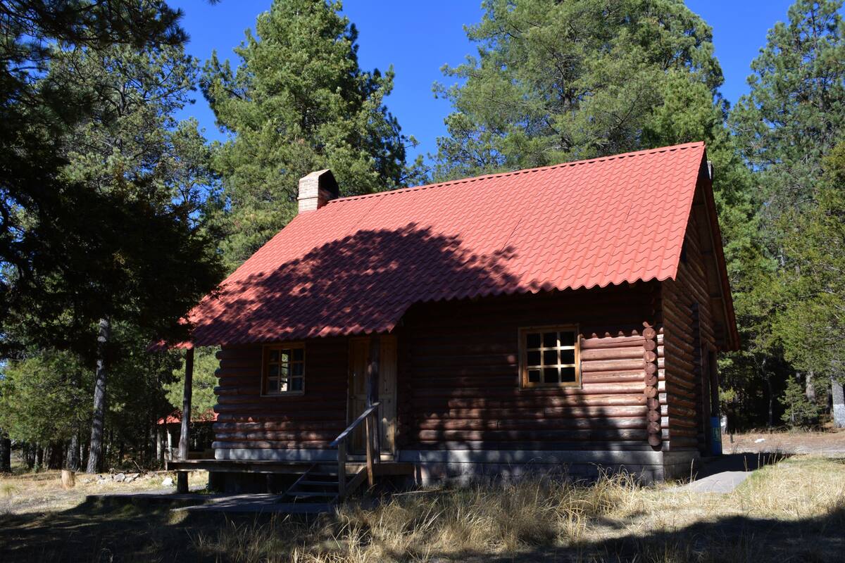 A log cabin with a red roof, wooden exterior, and a chimney.