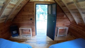 Quarto de sótão aconchegante, com teto inclinado, duas camas de madeira, um pequeno aquecedor e uma porta que dá para o exterior.