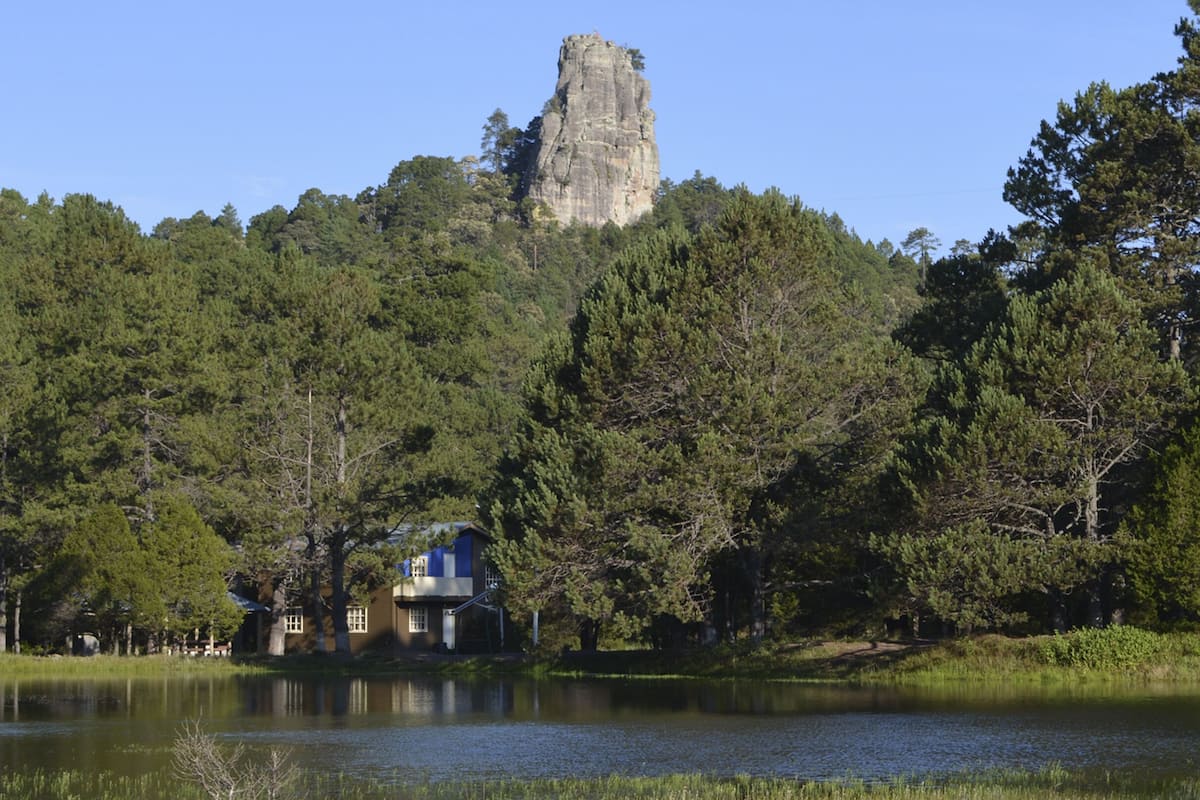A house by a lake with a prominent rock formation in the background.