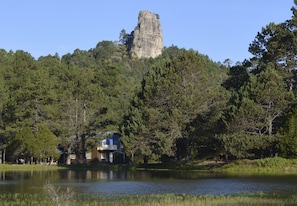 Une maison au bord d’un lac, avec une formation rocheuse imposante en arrière-plan.