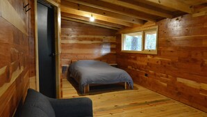 Quarto de cabana de madeira com uma cama, um sofá e uma janela.