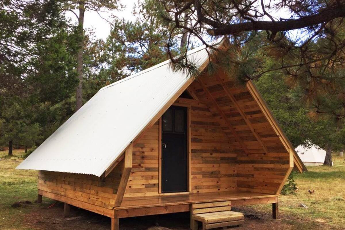 A small wooden cabin with a pitched roof and a door, surrounded by trees.