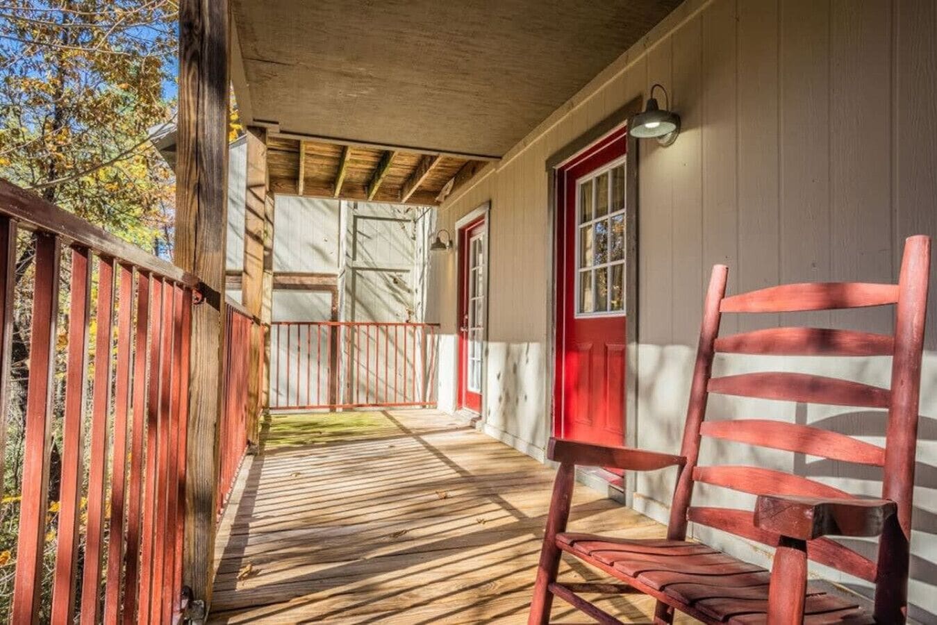 A wooden porch with a red chair, a red door, and a metal railing.