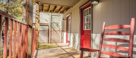 A wooden porch with a red chair, a red door, and a metal railing.