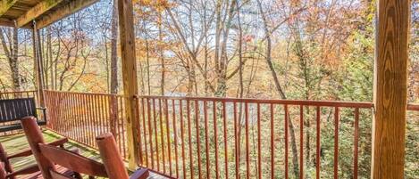 A wooden deck with a railing, benches, and a view of trees with autumn foliage.