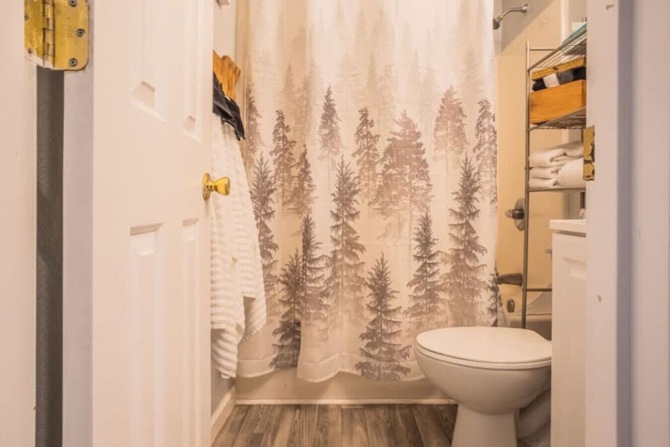 A bathroom with a shower curtain featuring a forest pattern, a toilet, and a shelf with towels.