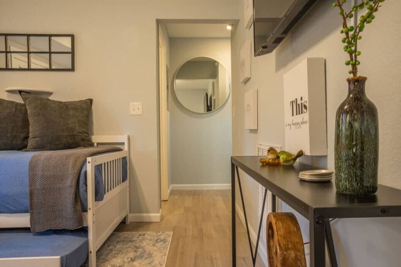 A bedroom with a bed, a dresser, a mirror, and a small table with a vase.