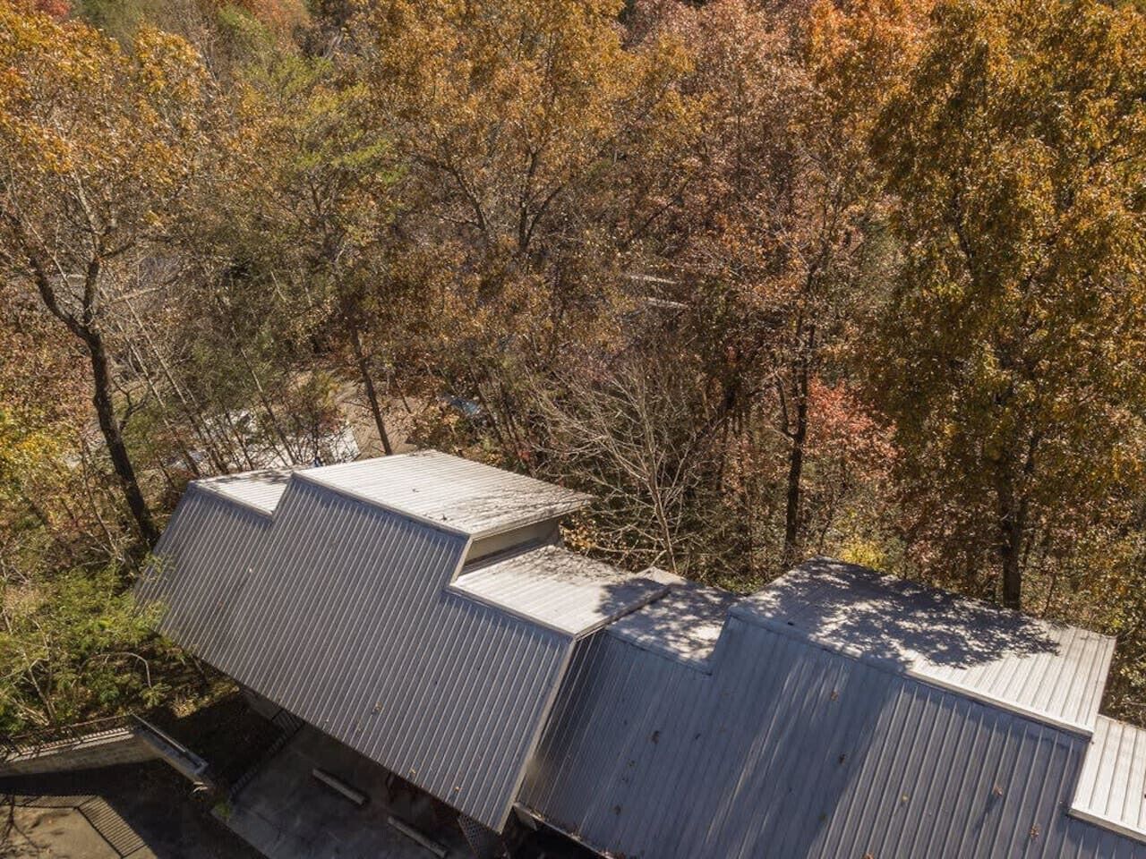 Un edifici amb teulada inclinada, envoltat d'arbres de fullatge tardà.
