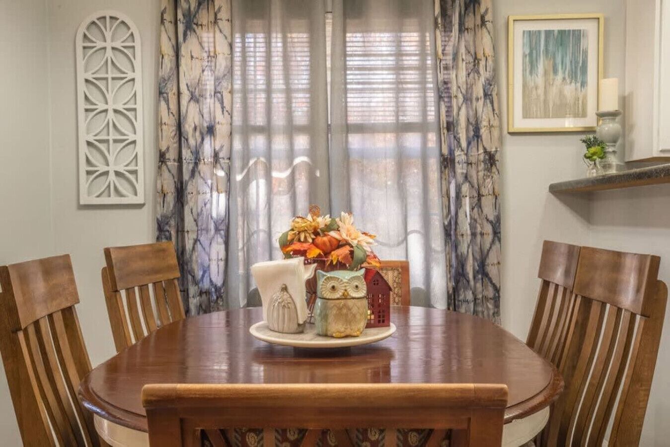 Mesa de jantar com arranjo floral, rodeada por cadeiras de madeira.