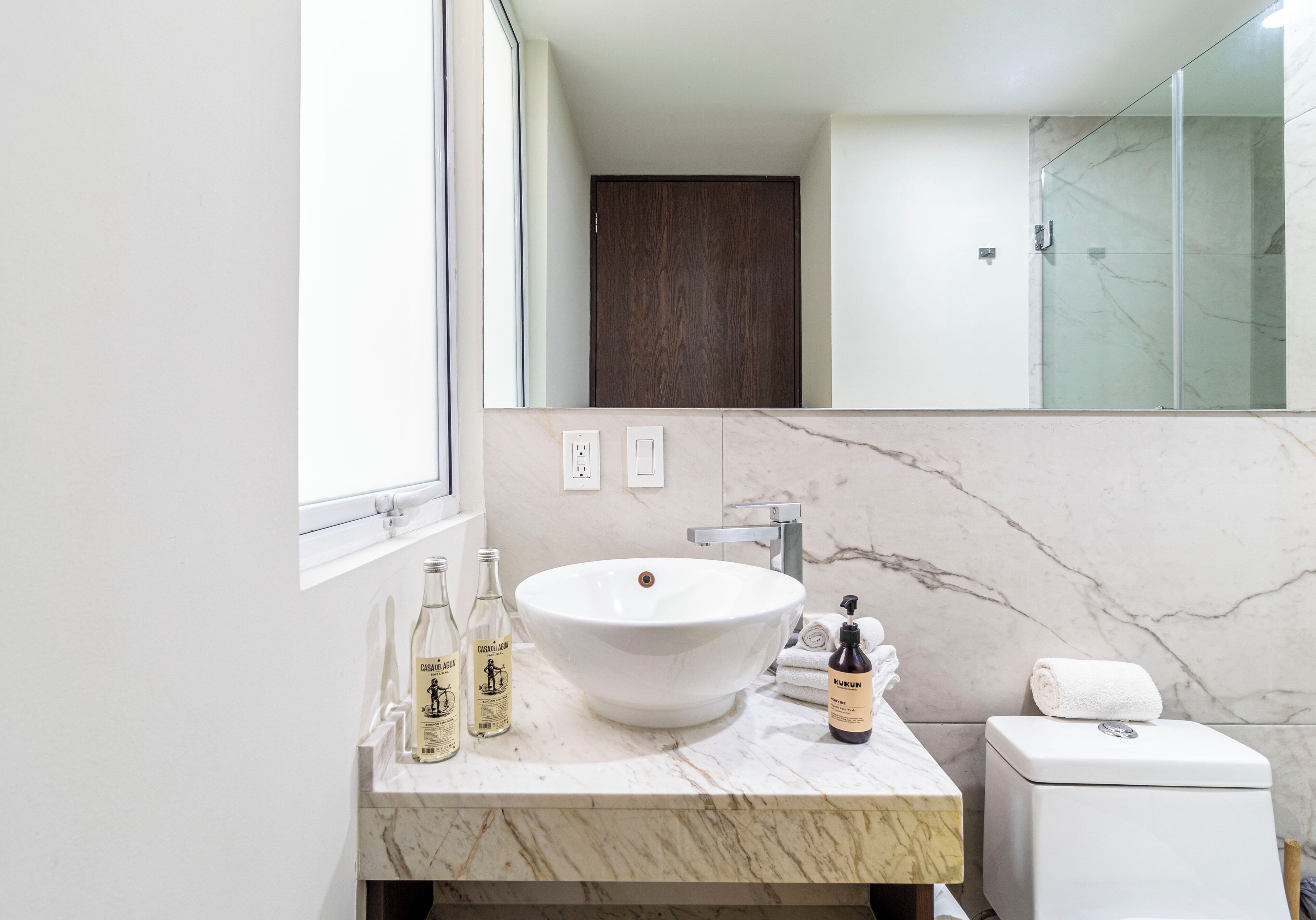 A bathroom with a large white sink, a glass shower enclosure, and a dark wooden door.
