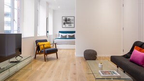 Een moderne woonkamer met een flatscreen televisie, een glazen salontafel en een bank met kussens.