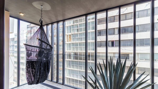 A room with large windows, a macrame hanging chair, and a tall plant. - Horacio by Kukun (Mexico City)