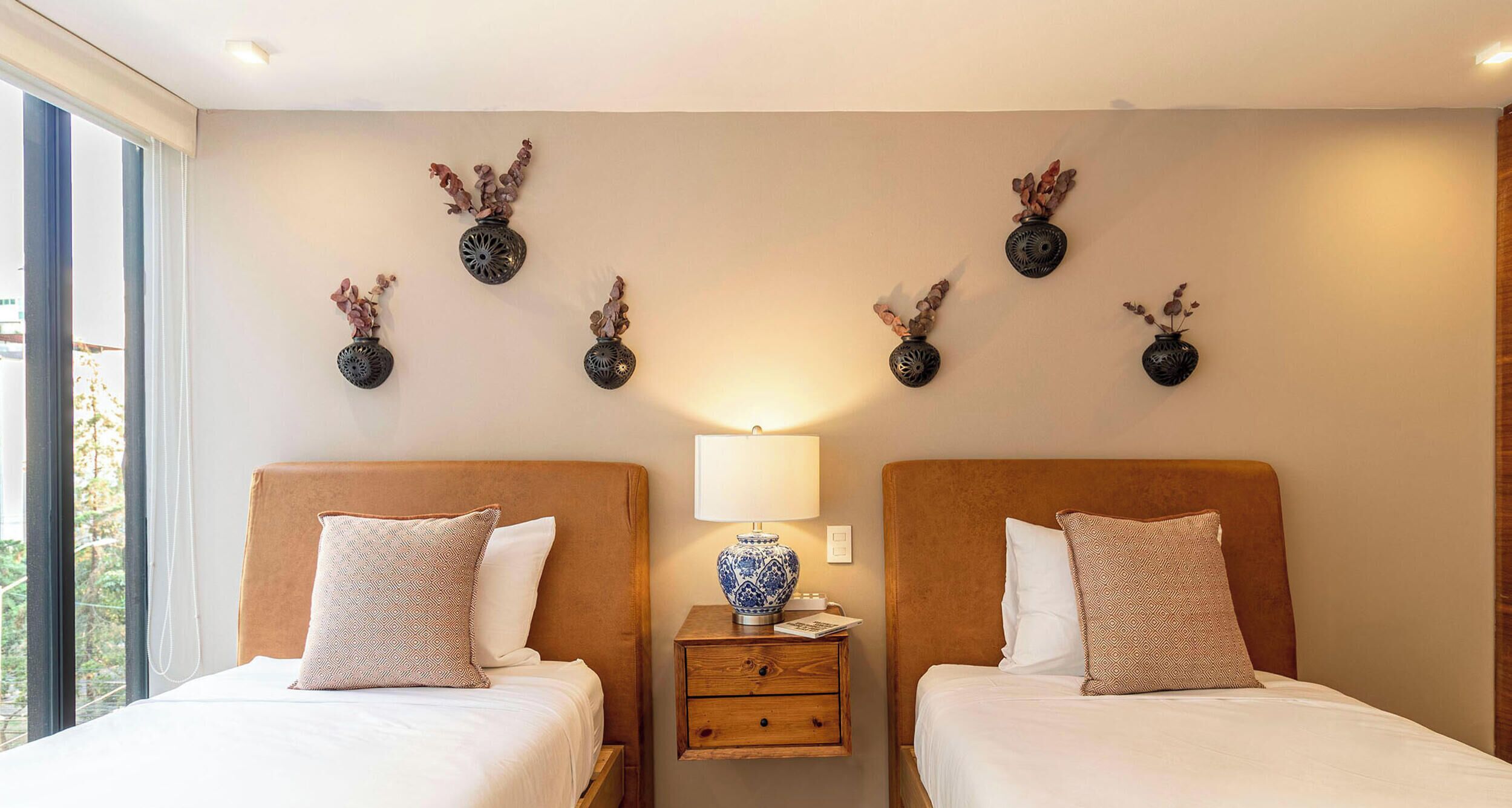 Une chambre d’hôtel avec deux lits, une table de chevet avec une lampe et des vases fixés au mur.