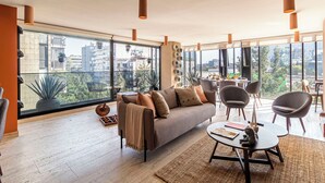 Una sala de estar moderna con un sofá, sillas, una mesa de centro y ventanas amplias que ofrecen vistas a la ciudad.