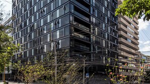 Un edificio moderno de varios pisos con fachada enrejada, rodeado de árboles y un cielo despejado.