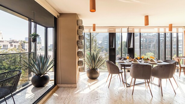 Un moderno comedor con un gran ventanal, plantas en macetas y una mesa dispuesta para dos.