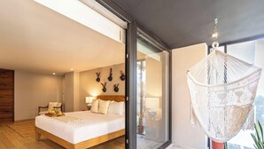 Un dormitorio moderno con una cama grande, lámparas de noche, una silla colgante de macramé y vistas a través de un ventanal.