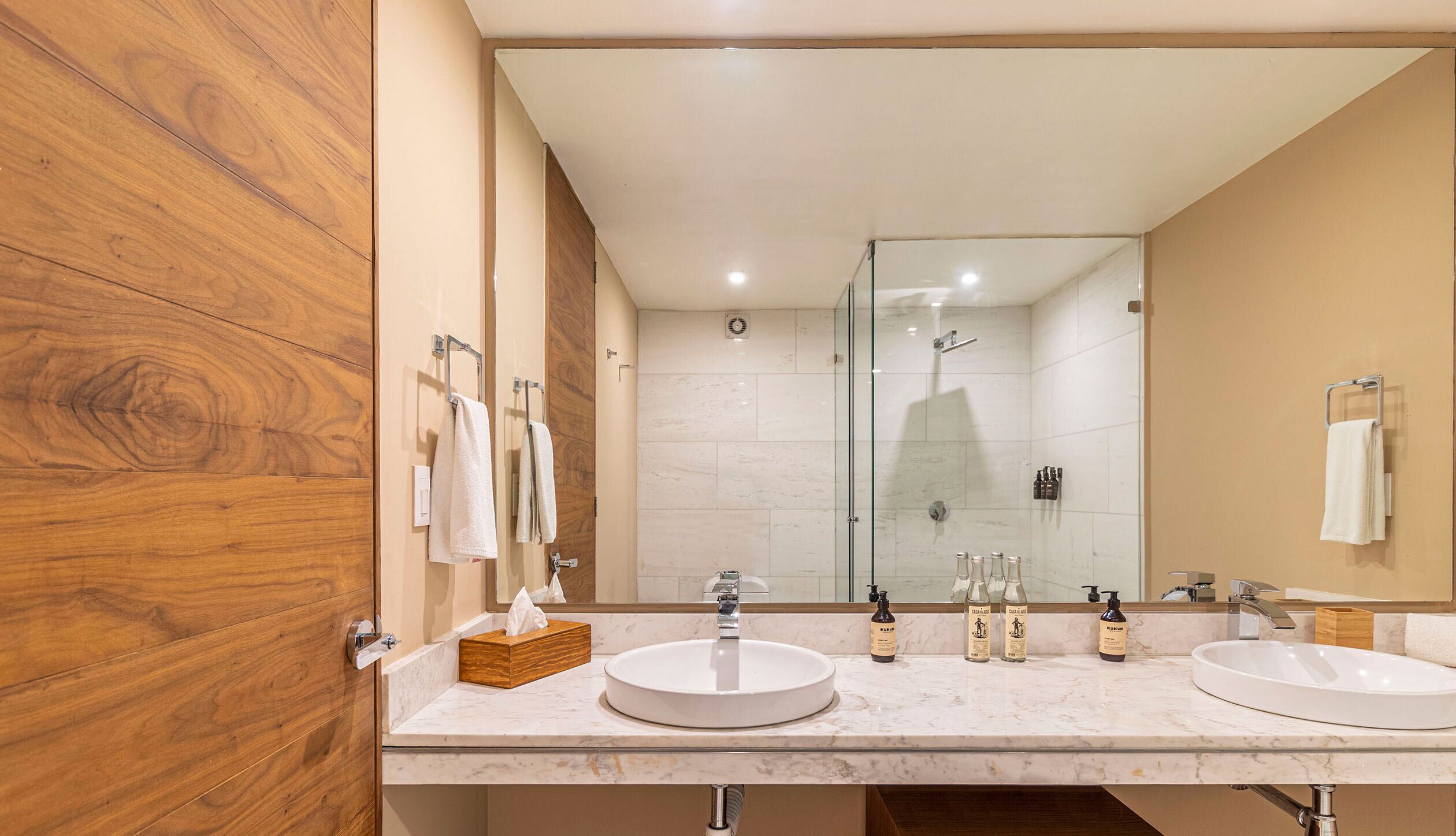 A modern bathroom with two sinks, a glass shower enclosure, and wooden paneling.