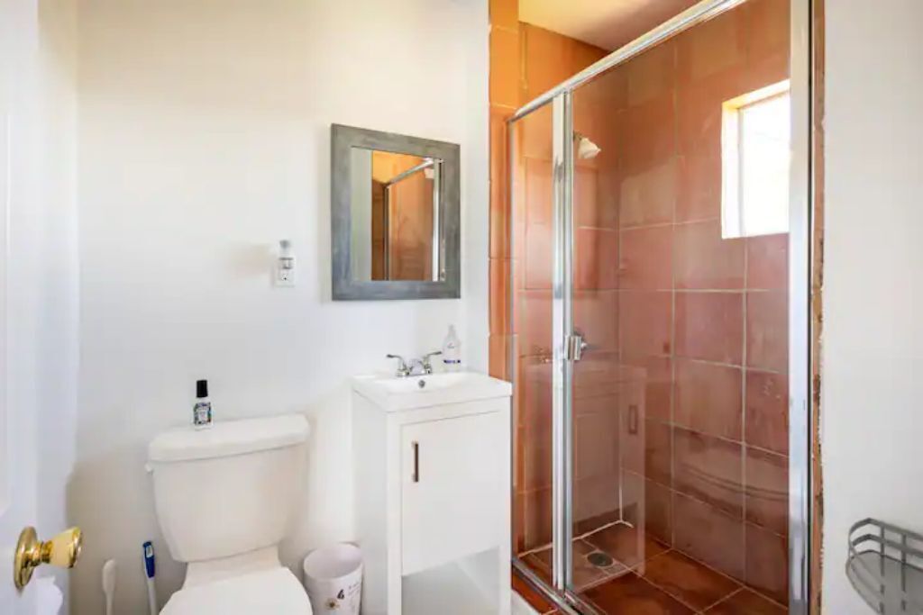 Et badeværelse med toilet, håndvask, spejl og brusekabine i glas.