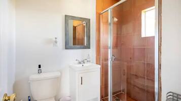 Et badeværelse med toilet, håndvask, spejl og brusekabine i glas.