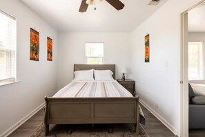 Une chambre à coucher avec un lit, une table de chevet, un ventilateur de plafond et des œuvres d’art accrochées aux murs.