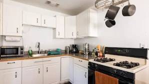 Una cocina con armarios blancos, microondas, estufa y ollas colgantes.