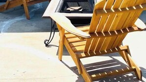 Una silla Adirondack de madera y una mesa metálica con una parrilla en el centro, frente a una pared azul.