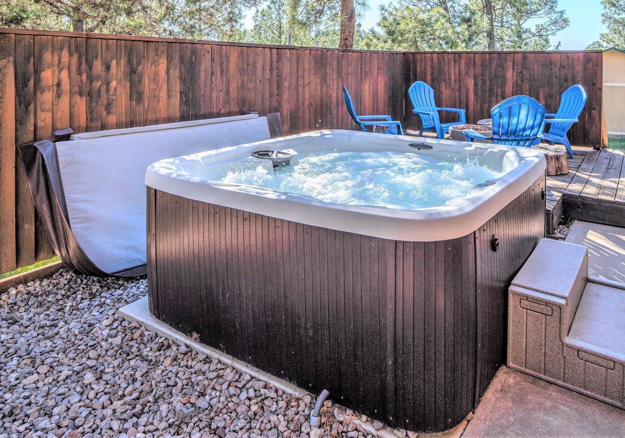A hot tub with a wooden deck, surrounded by blue chairs and a stone table.